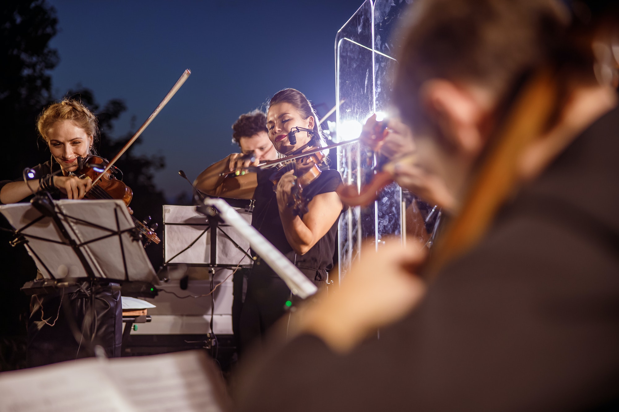 Violin players playing in orchestra at night outdoor concert